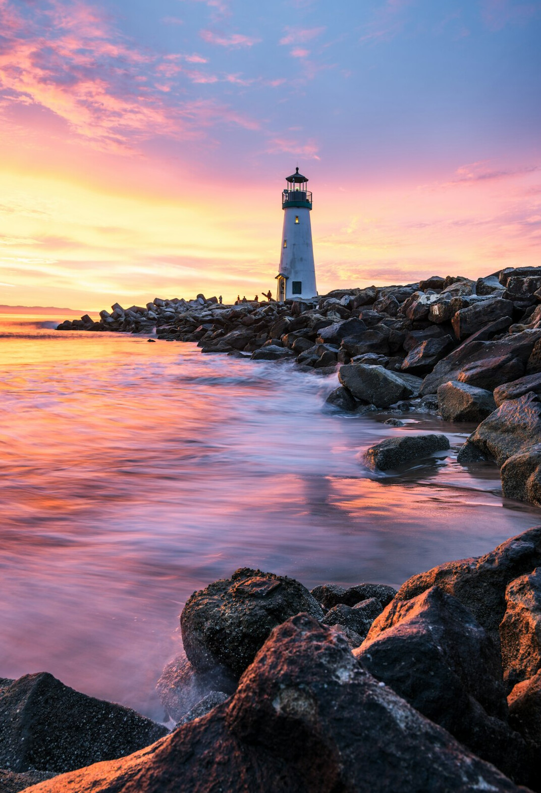 White lighthouse on a rocky coast at sunset