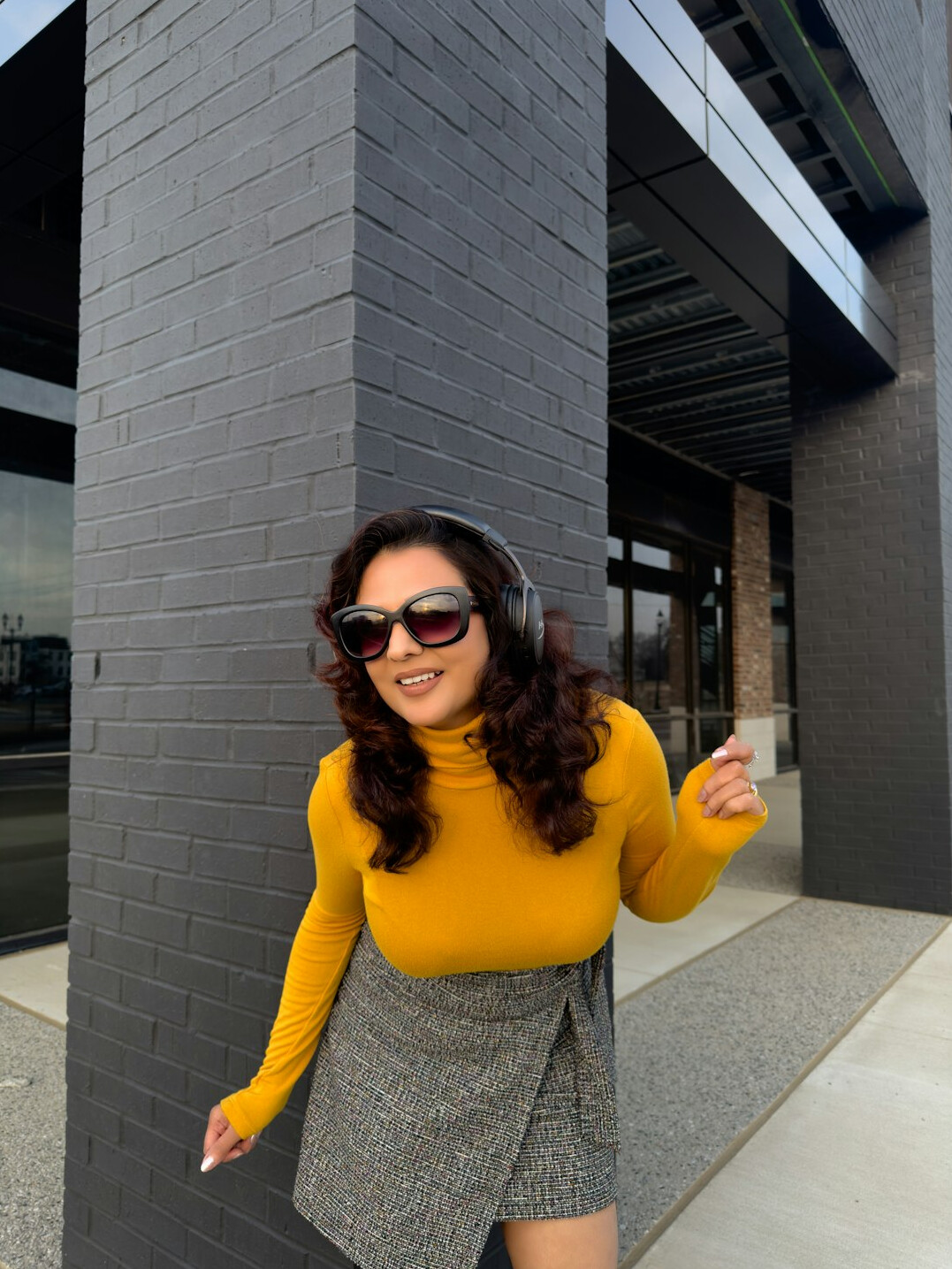 Smiling Latina woman journalist in her thirties wearing a mustard sweater giving thumbs up